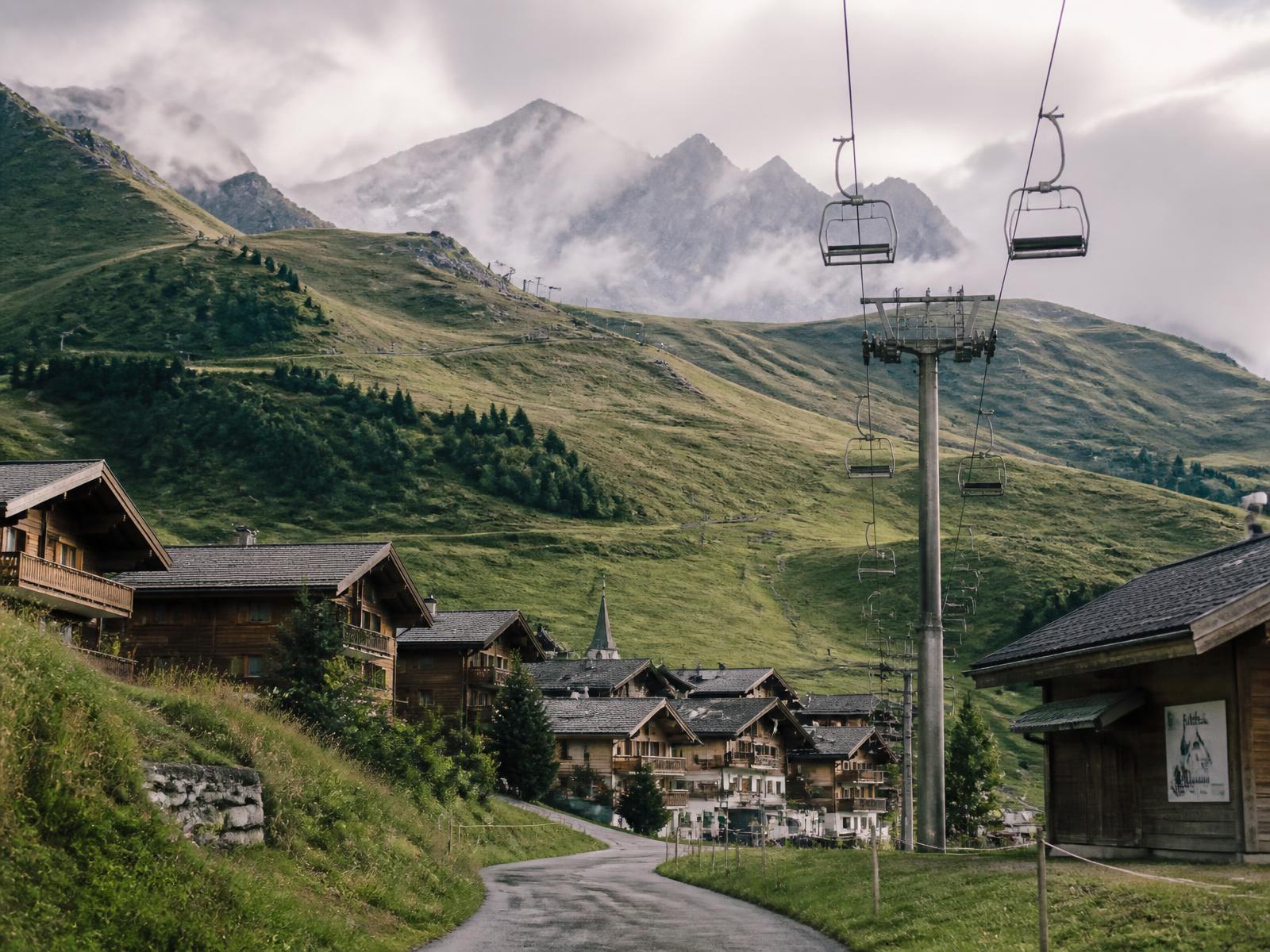 Alpine resort village in summer with still chairlift cables running above green slopes and chalets
